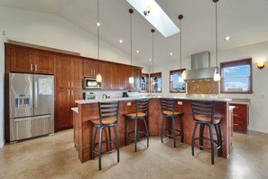 Cocina moderna con armarios de madera, electrodomésticos de acero inoxidable y una isla central con taburetes de bar.