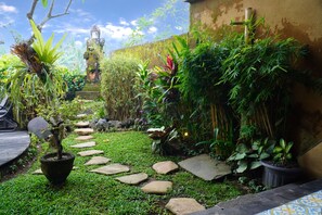A garden with a variety of plants, a stone pathway, and a statue.