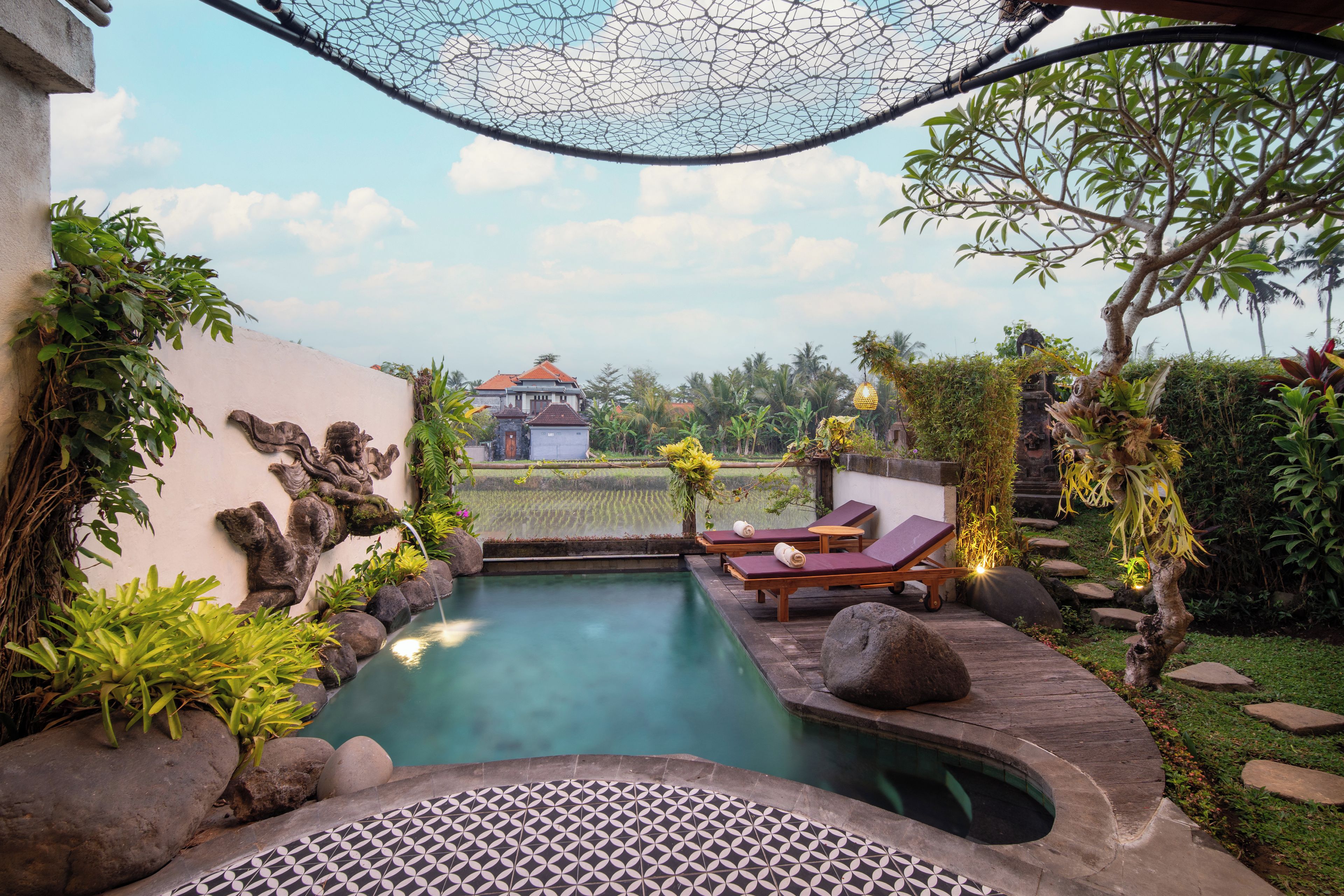 Área da piscina com espreguiçadeiras, um painel decorativo e vista para um edifício ao longe.