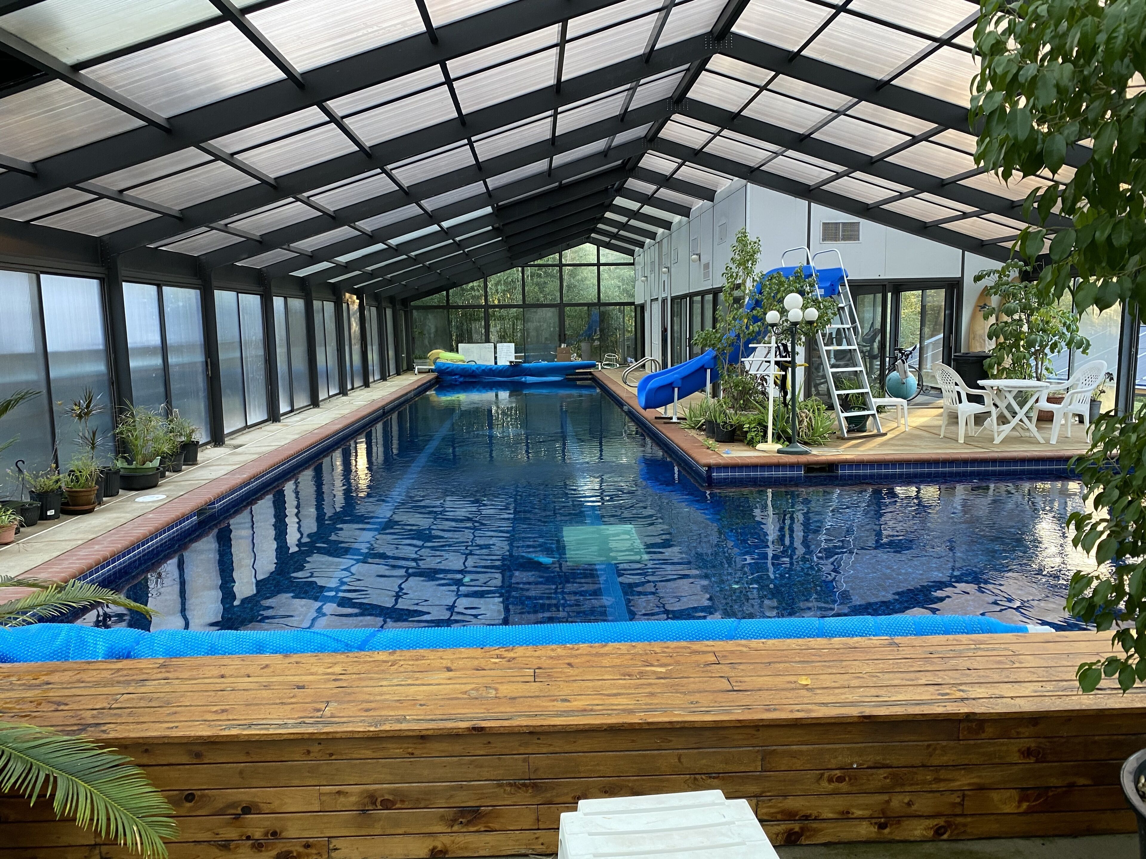 Ein Innenpool mit Rutsche, umgeben von Topfpflanzen und einer Holzterrasse.