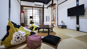 Een traditionele Japanse kamer met tatami vloeren, een lage tafel, kussens, een televisie en een schuifdeur.