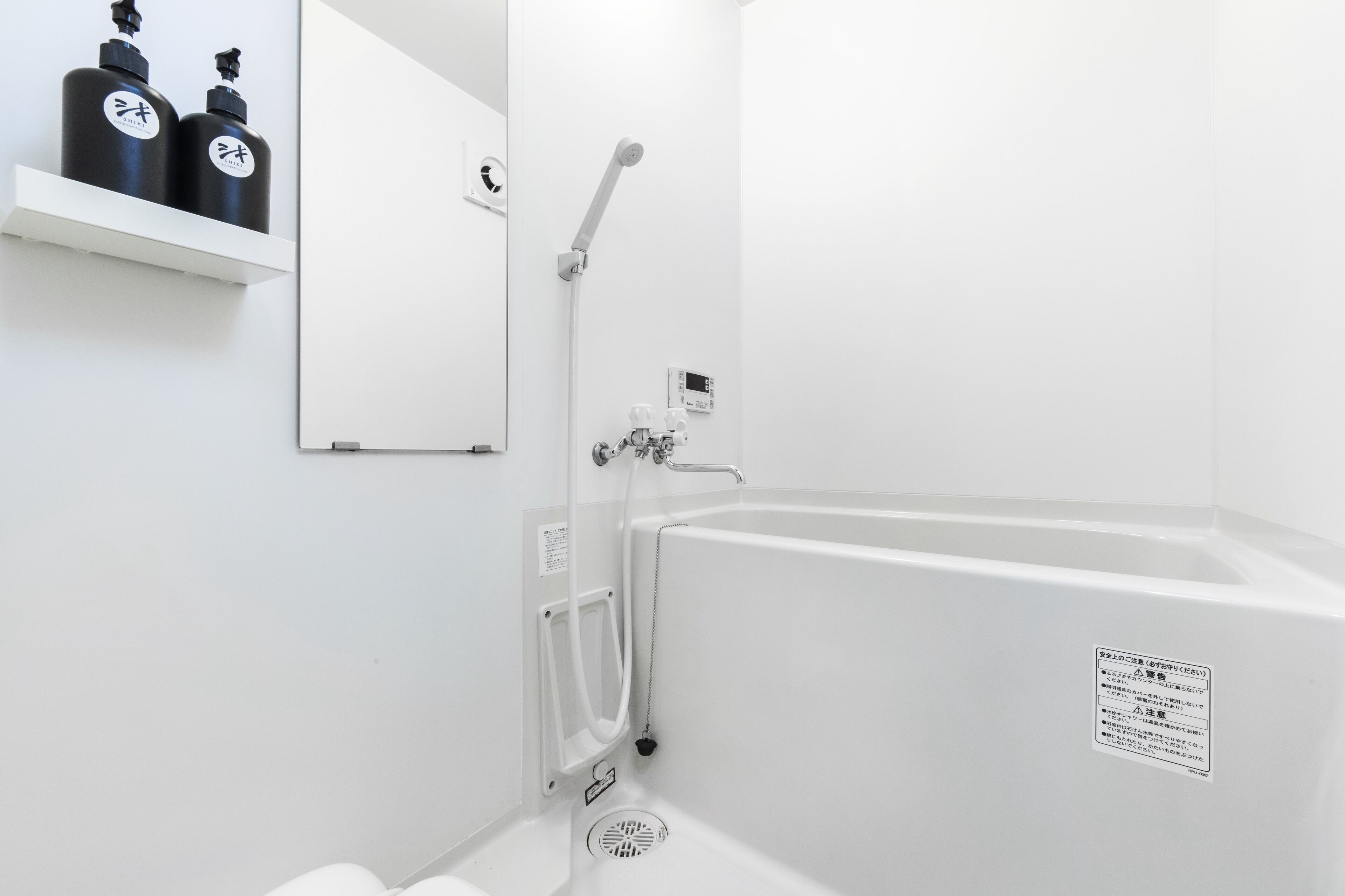 Une salle de bain moderne avec une baignoire blanche, une douchette à main et deux bouteilles noires posées sur une étagère blanche.