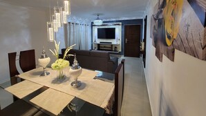 Un comedor con una mesa preparada para cuatro personas, una araña y un sofá al fondo.