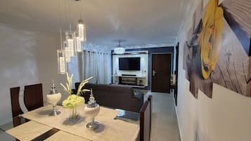 Un coin repas avec une table dressée pour quatre personnes, un lustre et un canapé en arrière-plan.