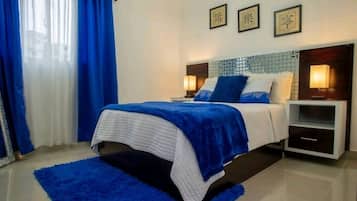 Une chambre à coucher avec un lit, des rideaux bleus, une table de chevet et des œuvres d’art mural.
