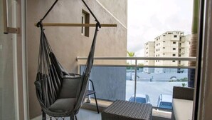 Un balcón con una silla colgante, mobiliario de mimbre y vistas a edificios.