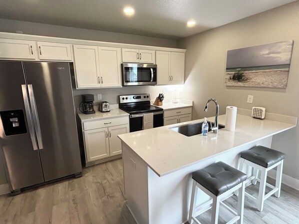 A modern kitchen with stainless steel appliances, a central island with bar stools, and a painting on the wall. - Relaxing Entire House in Ankeny, IA (Bondurant)