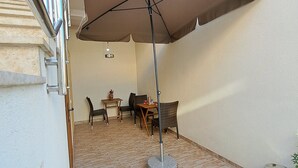 Eine Terrasse im Freien mit Tisch, Stühlen, einem großen Sonnenschirm und einem Mülleimer.