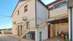 Ein zweistöckiges Wohngebäude mit Balkon, Treppe und einer kleinen Außen-Sitzgelegenheit.
