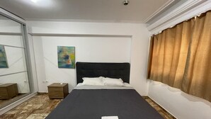 Una habitación de hotel con una cama grande, una mesita de noche, un cuadro en la pared y una ventana con cortinas.