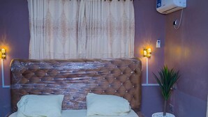 A bedroom with a wooden headboard, two bedside lamps, a potted plant, and an air conditioning unit. - captivating 3-bed House in Ibadan oyo-state nigeri (Oyo state Nigeria)