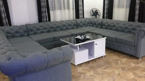 A grey sectional sofa with a white side table and a black coffee table in a room with a herringbone floor pattern and black curtains. - captivating 3-bed House in Ibadan oyo-state nigeri (Oyo state Nigeria)
