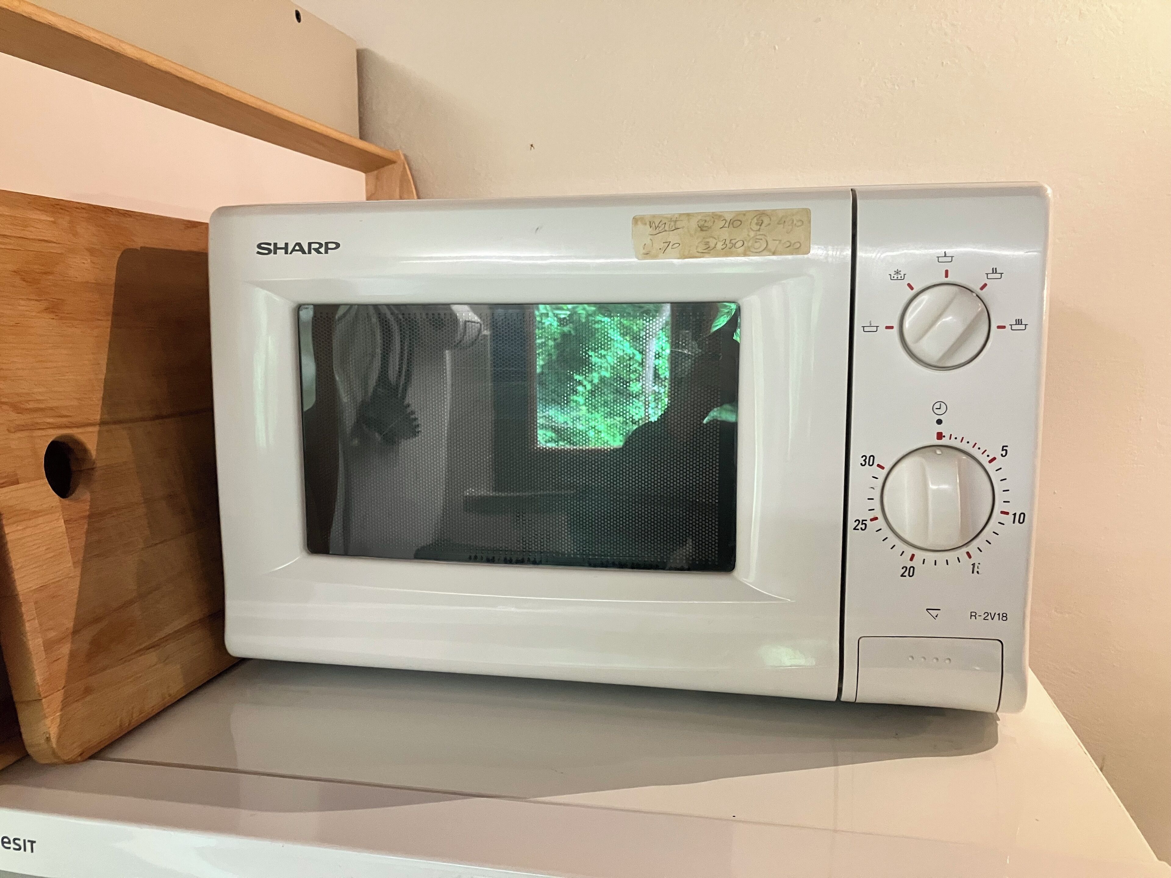 Eine weiße Sharp-Mikrowelle mit digitaler Anzeige steht auf einer weißen Arbeitsplatte neben einem Holzschrank.