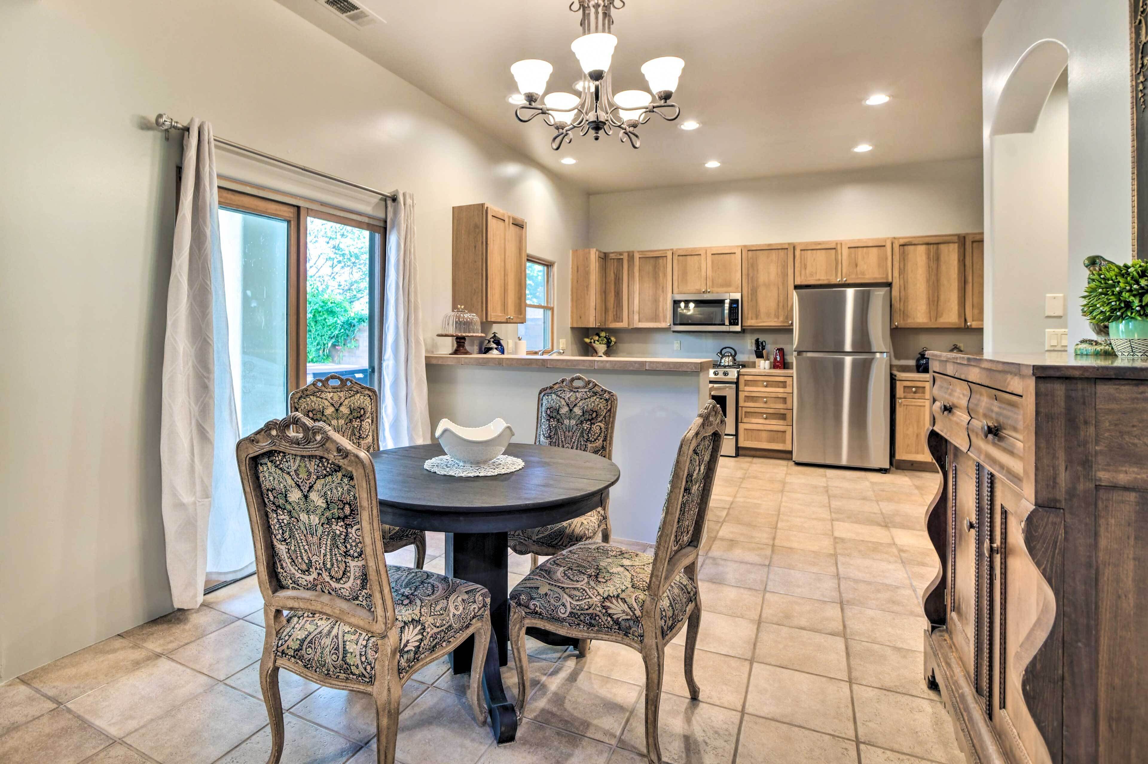 A modern kitchen with wooden cabinets, a stainless steel refrigerator, and a dining area with patterned chairs and a round table.