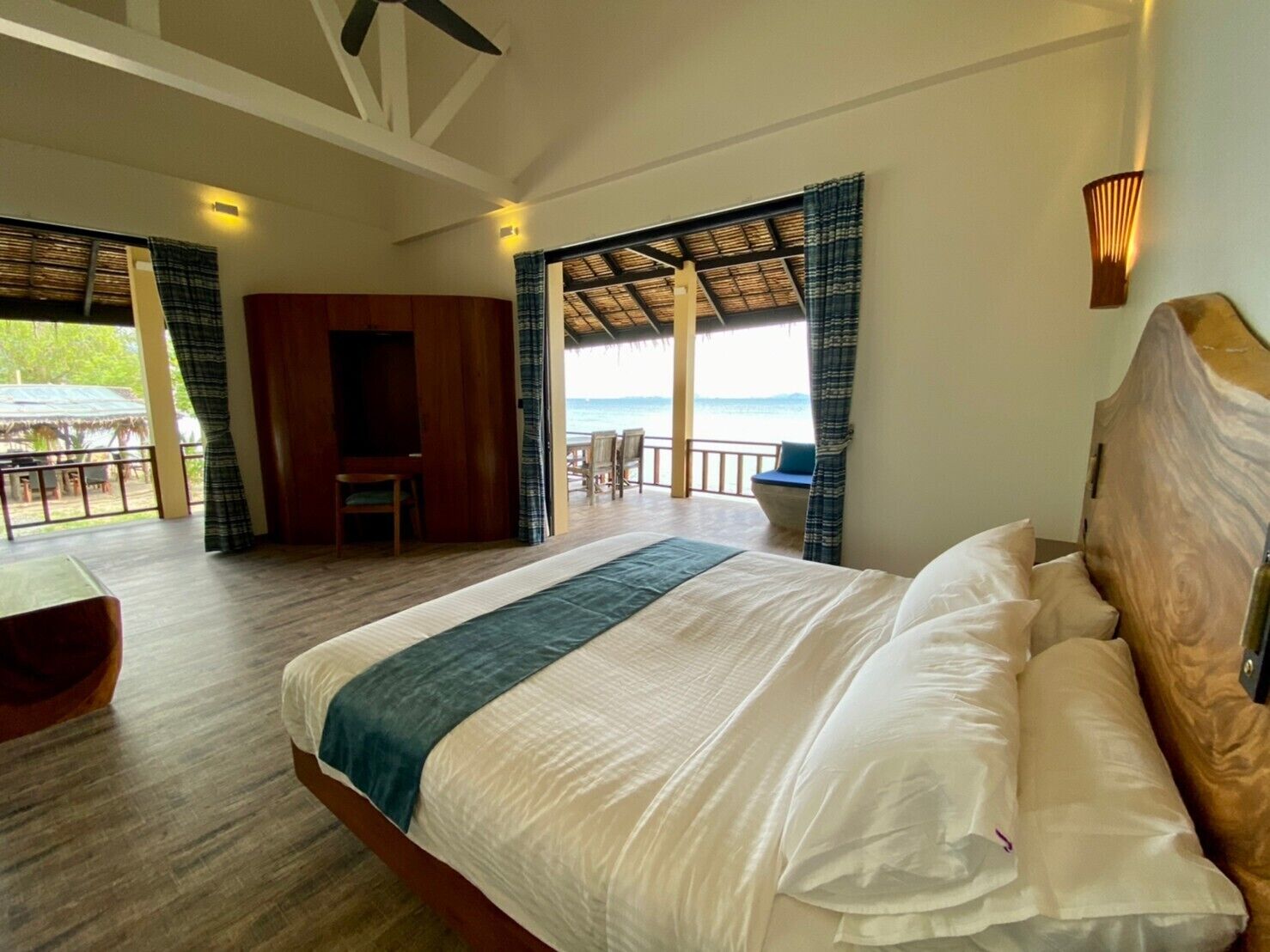 A bedroom with a large bed, wooden headboard, and a view of the beach.