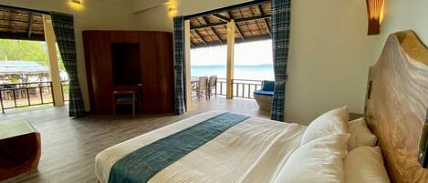 A bedroom with a large bed, wooden headboard, and a view of the beach.