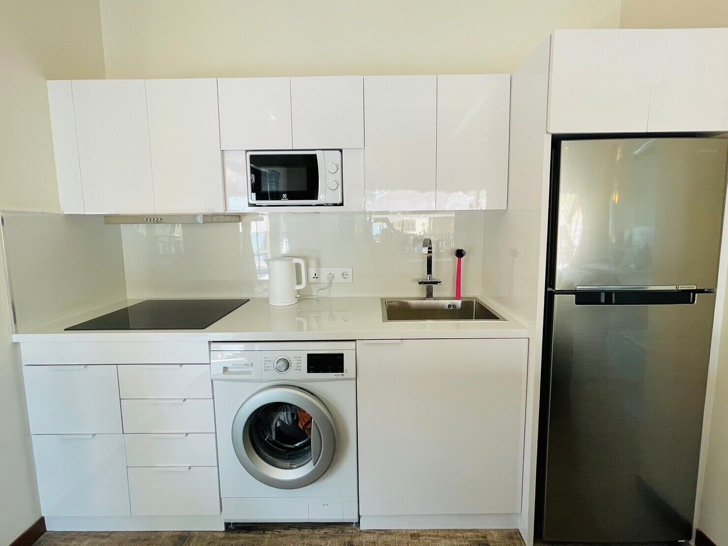 A compact kitchenette with a microwave, sink, washing machine, and refrigerator.
