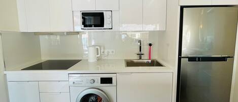 A compact kitchenette with a microwave, sink, washing machine, and refrigerator.