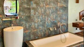 A bathroom with a large bathtub, a round sink, and a mirror.