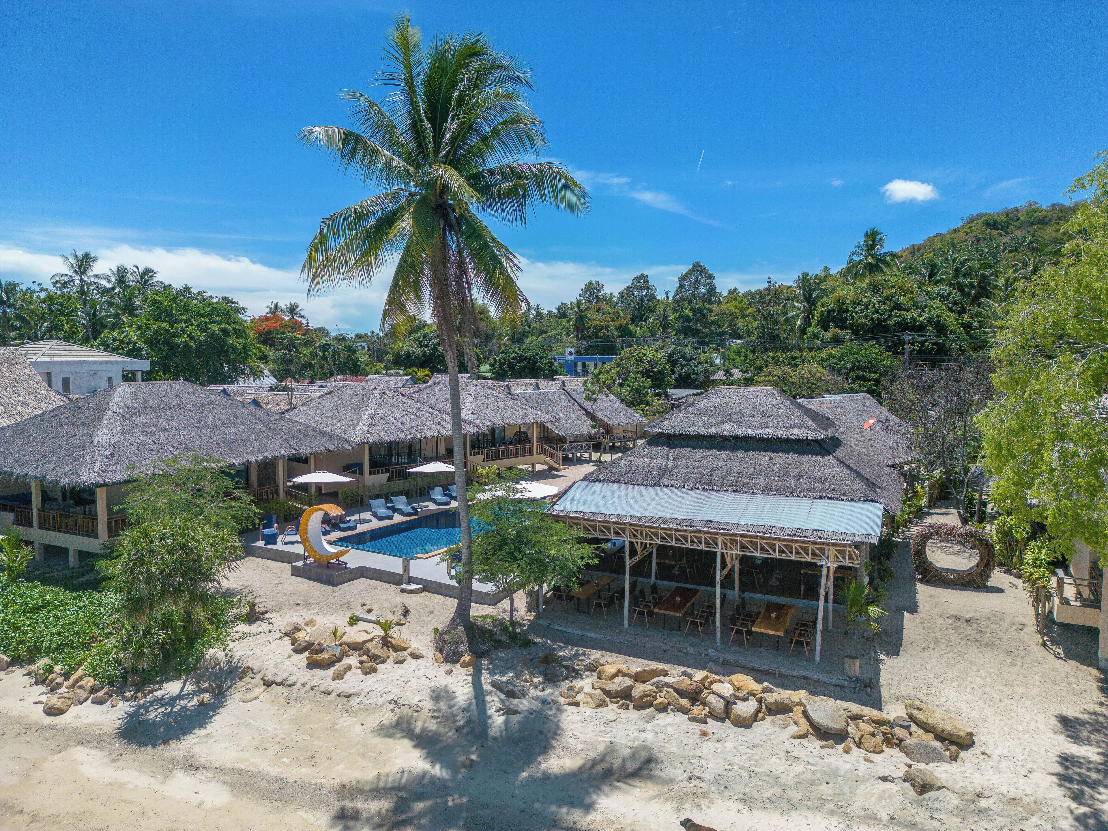 A resort with thatched-roof buildings, a swimming pool, and a sandy beach area.