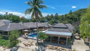 A resort with thatched-roof buildings, a swimming pool, and a sandy beach area.