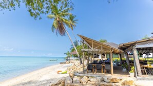 A beachside restaurant with outdoor seating, a thatched roof, and a view of the ocean. - Absolute Beachfront Resort (Ko Pha-ngan)