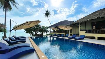 A poolside area with lounge chairs and umbrellas, a clear sky, and a view of the sea.