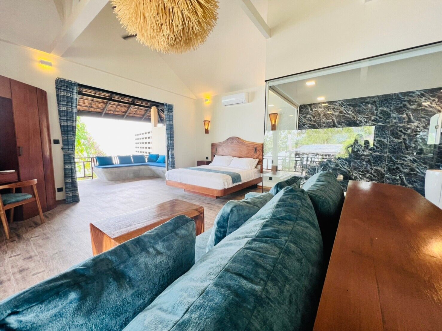 A spacious room with a large bed, a sofa, a wooden table, and a balcony with a view.