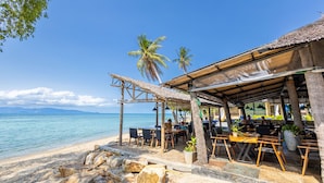 A beachside restaurant with outdoor seating, palm trees, and a view of the sea. - Absolute Beachfront Resort (Ko Pha-ngan)