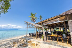 A beachside restaurant with outdoor seating, palm trees, and a view of the sea.