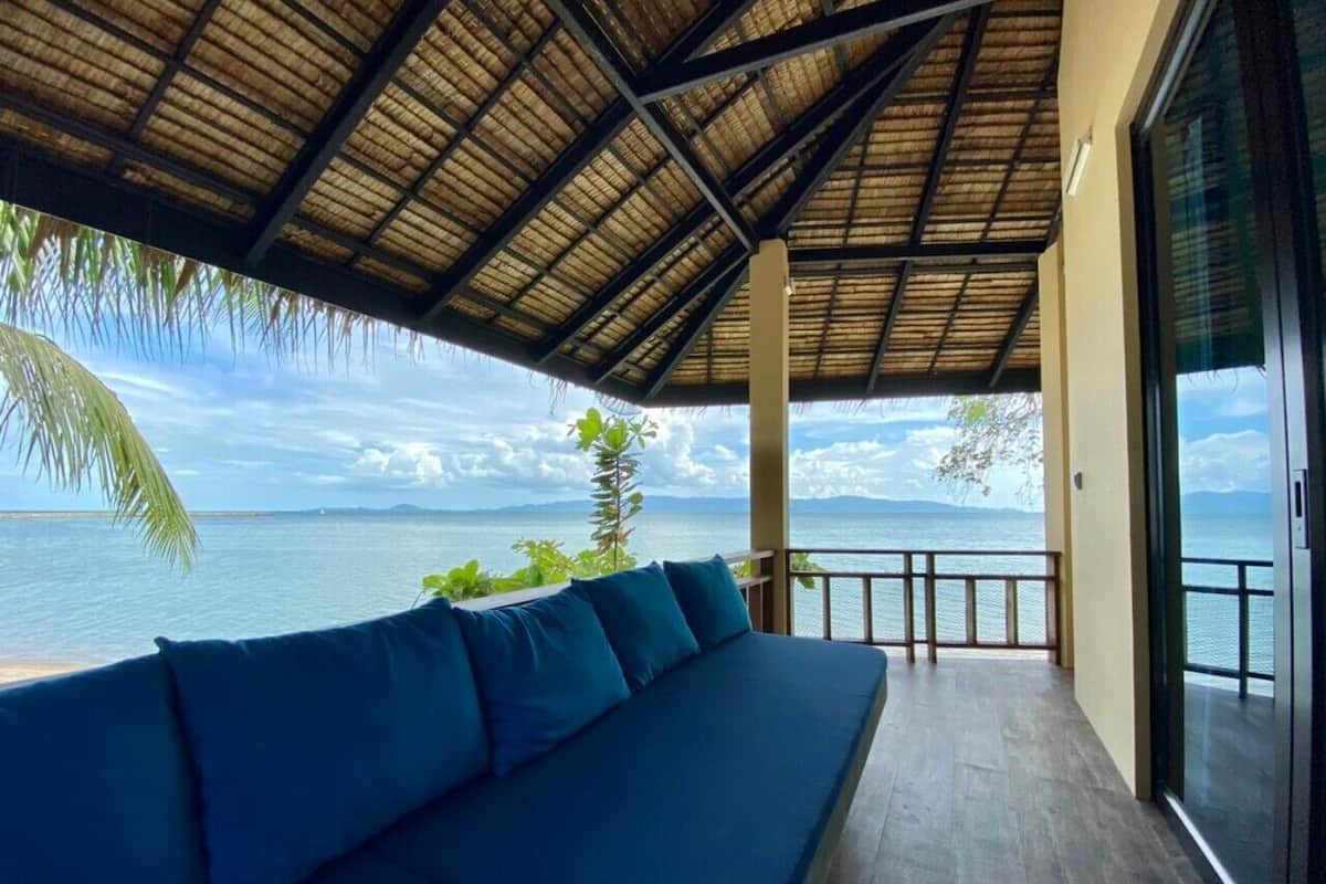 A balcony with a blue sofa, a thatched roof, and a view of the sea.