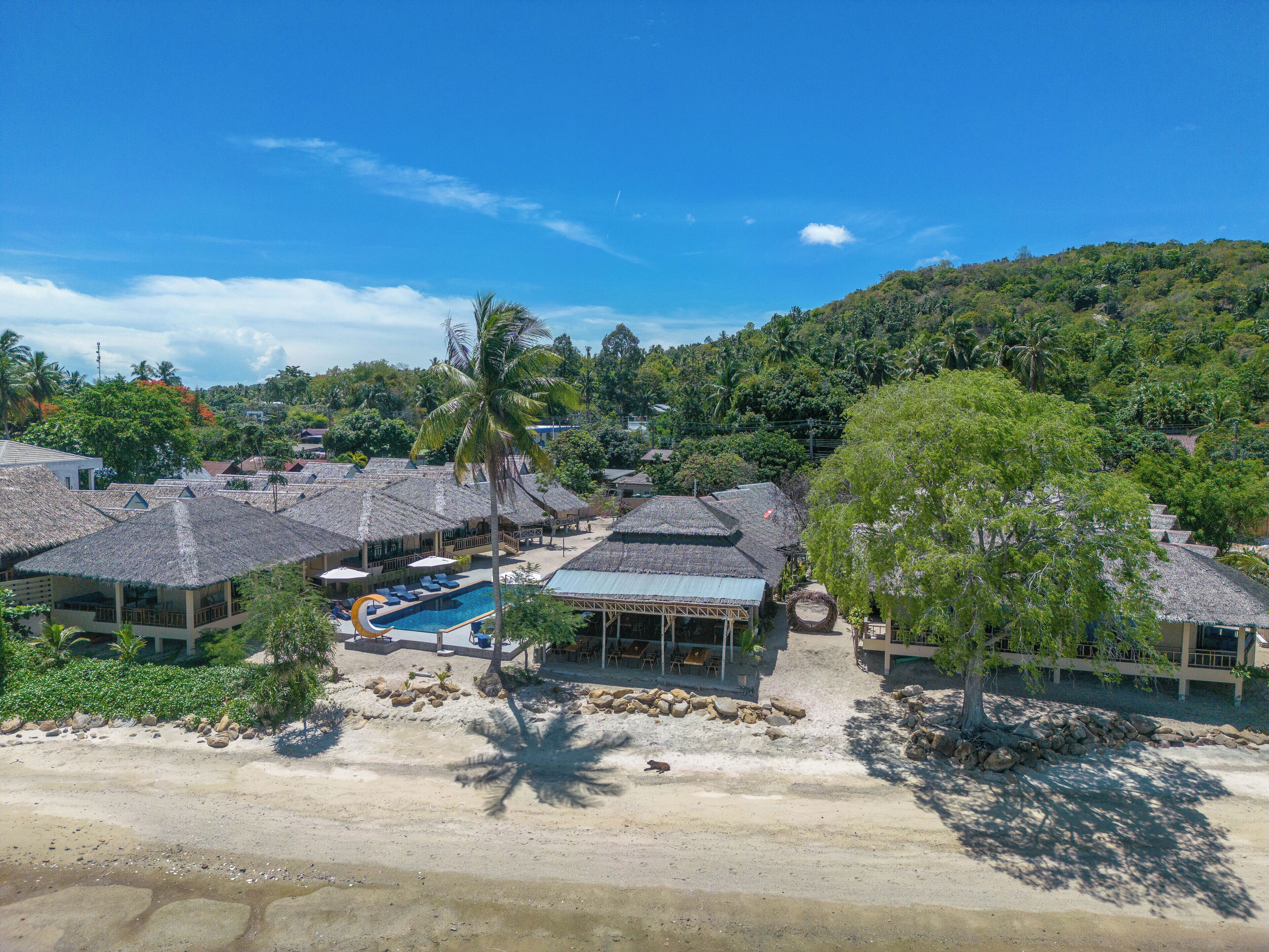 A resort with multiple thatched-roof buildings, a swimming pool, and a beach area.