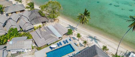 A resort with a swimming pool, beach, and thatched-roof buildings.