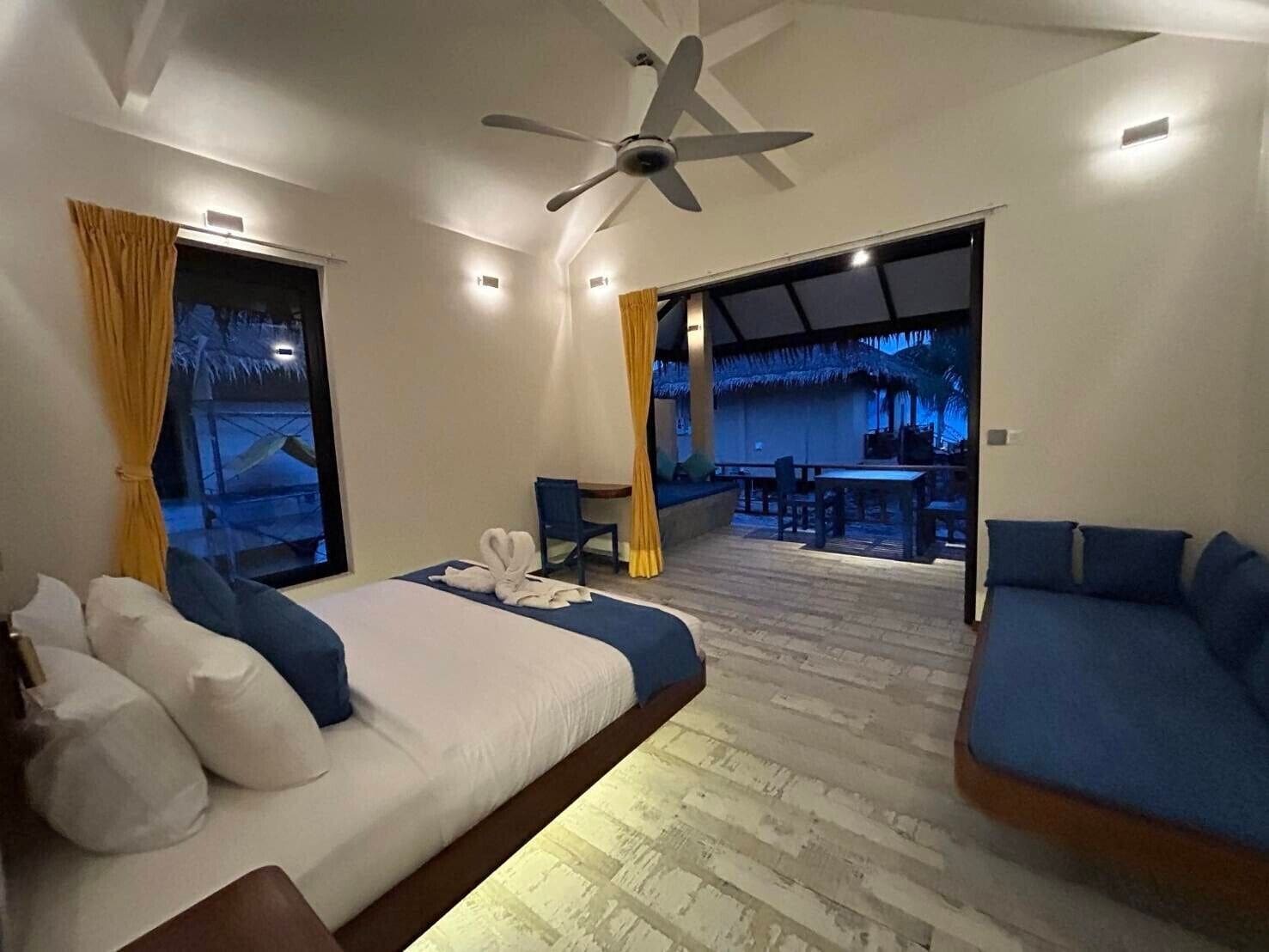 Quarto de hotel com cama, sofá, escrivaninha e área de jantar com mesas e cadeiras.