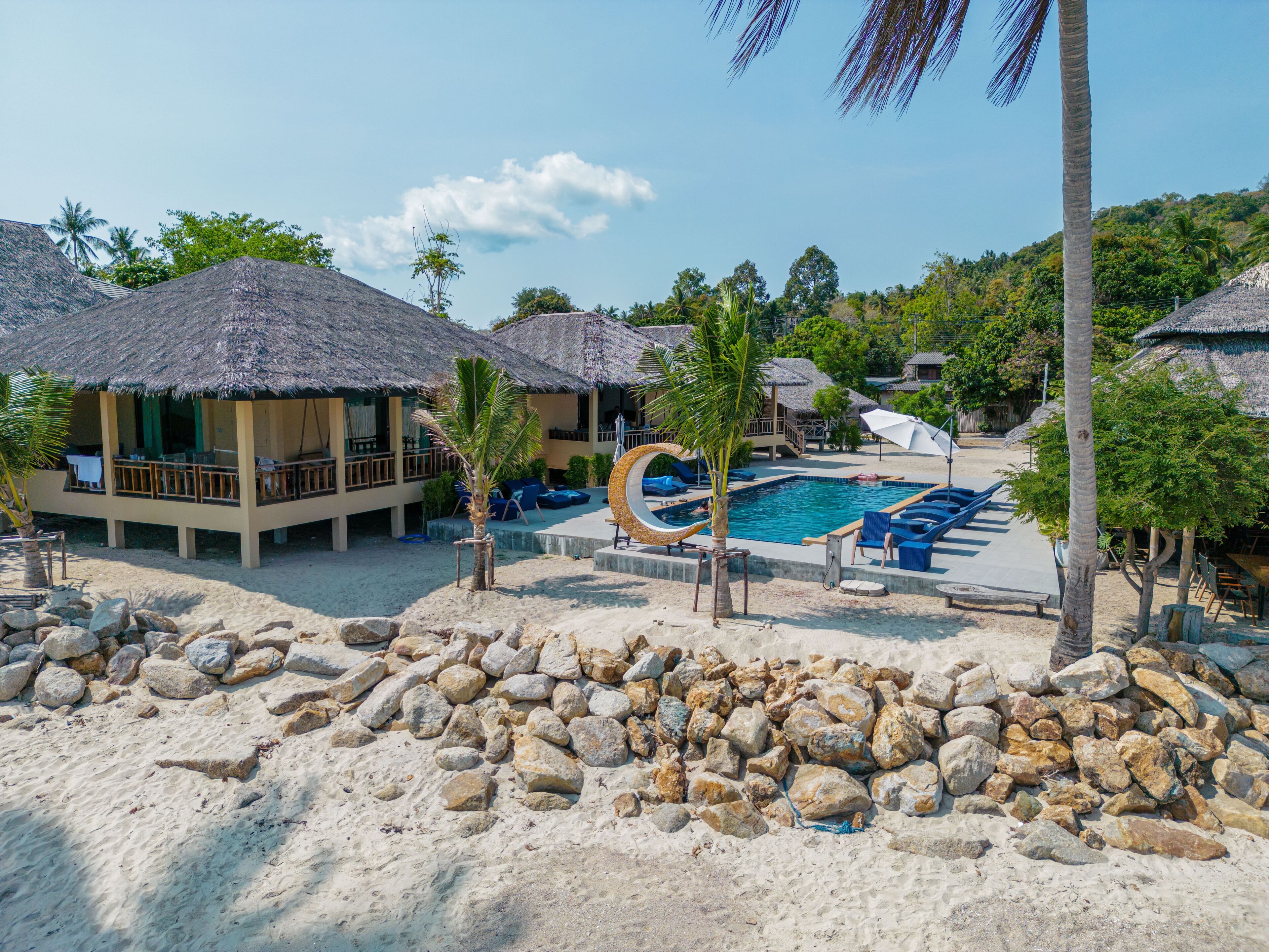 A resort with thatched-roof bungalows, a pool area, and a sandy beach.