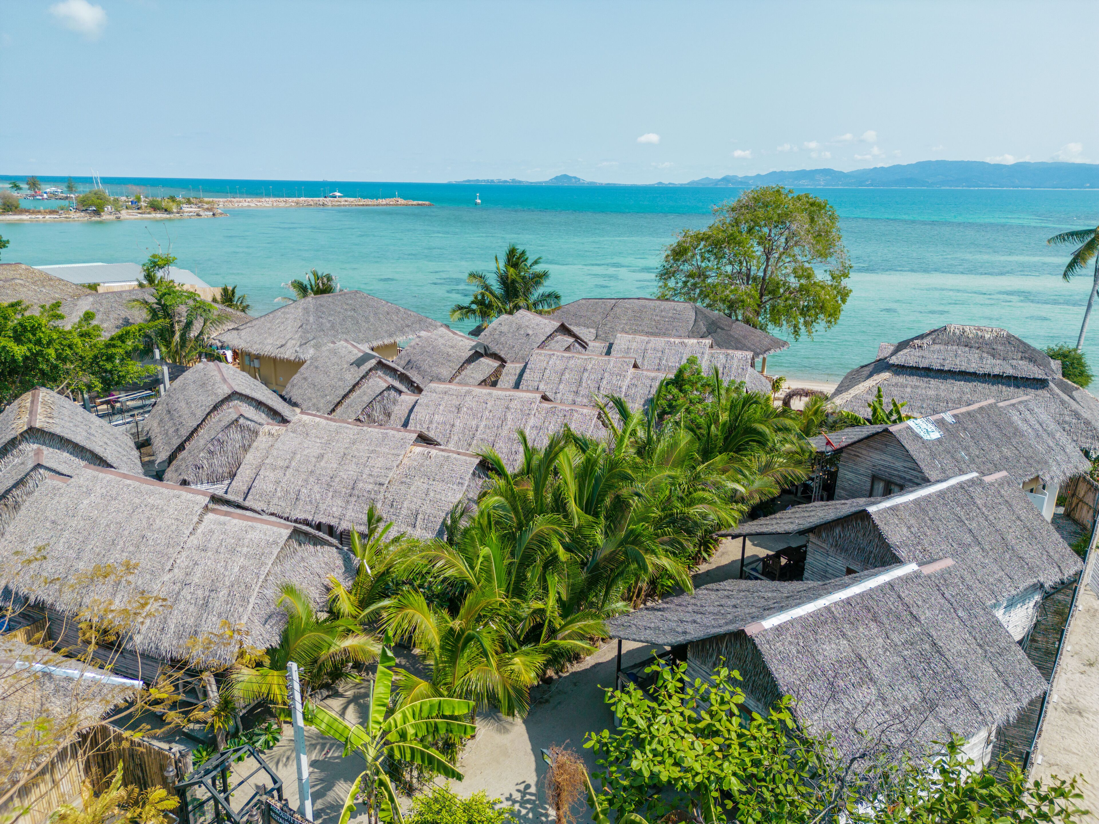 Ein Resort mit strohgedeckten Hütten, Palmen und Blick aufs Meer.
