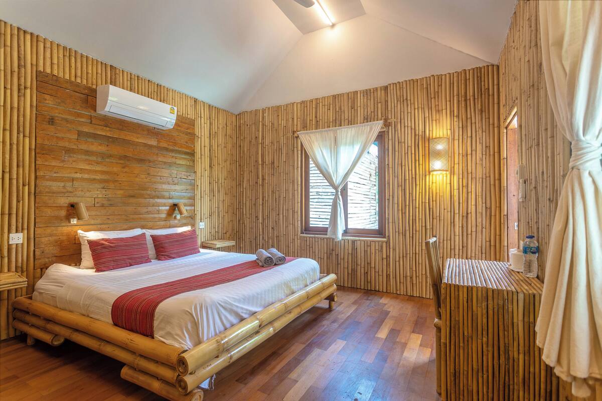 A room with a bed, a window with curtains, a bedside table, and a wall-mounted air conditioner.
