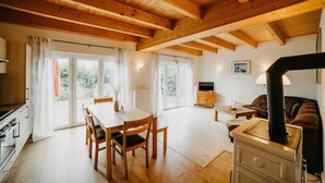 Una habitación acogedora con techo de madera, una mesa de comedor con sillas, un sofá, un televisor y una estufa.