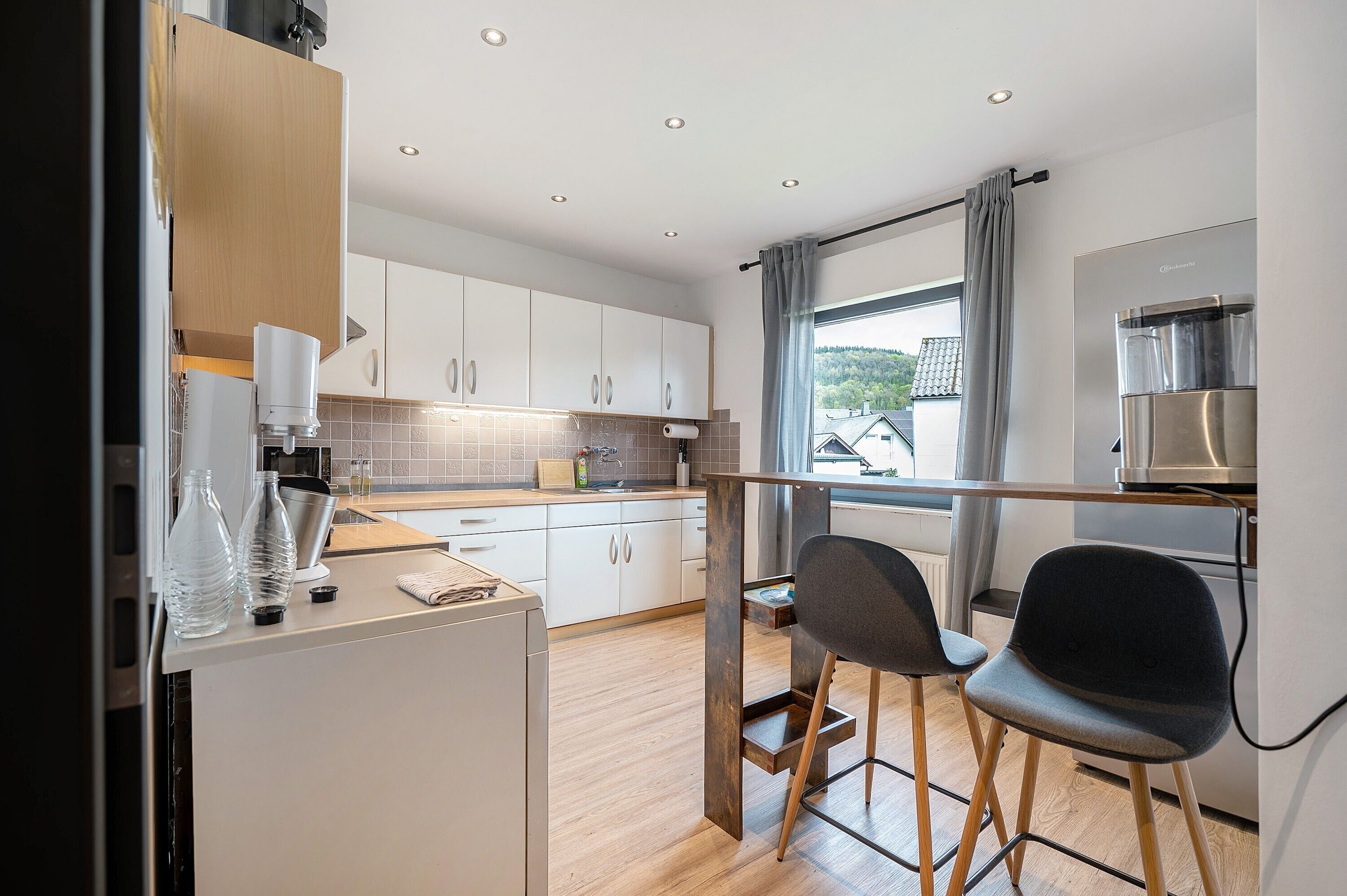 A modern kitchen with white cabinets, a built-in stove, and a window with a view of houses.