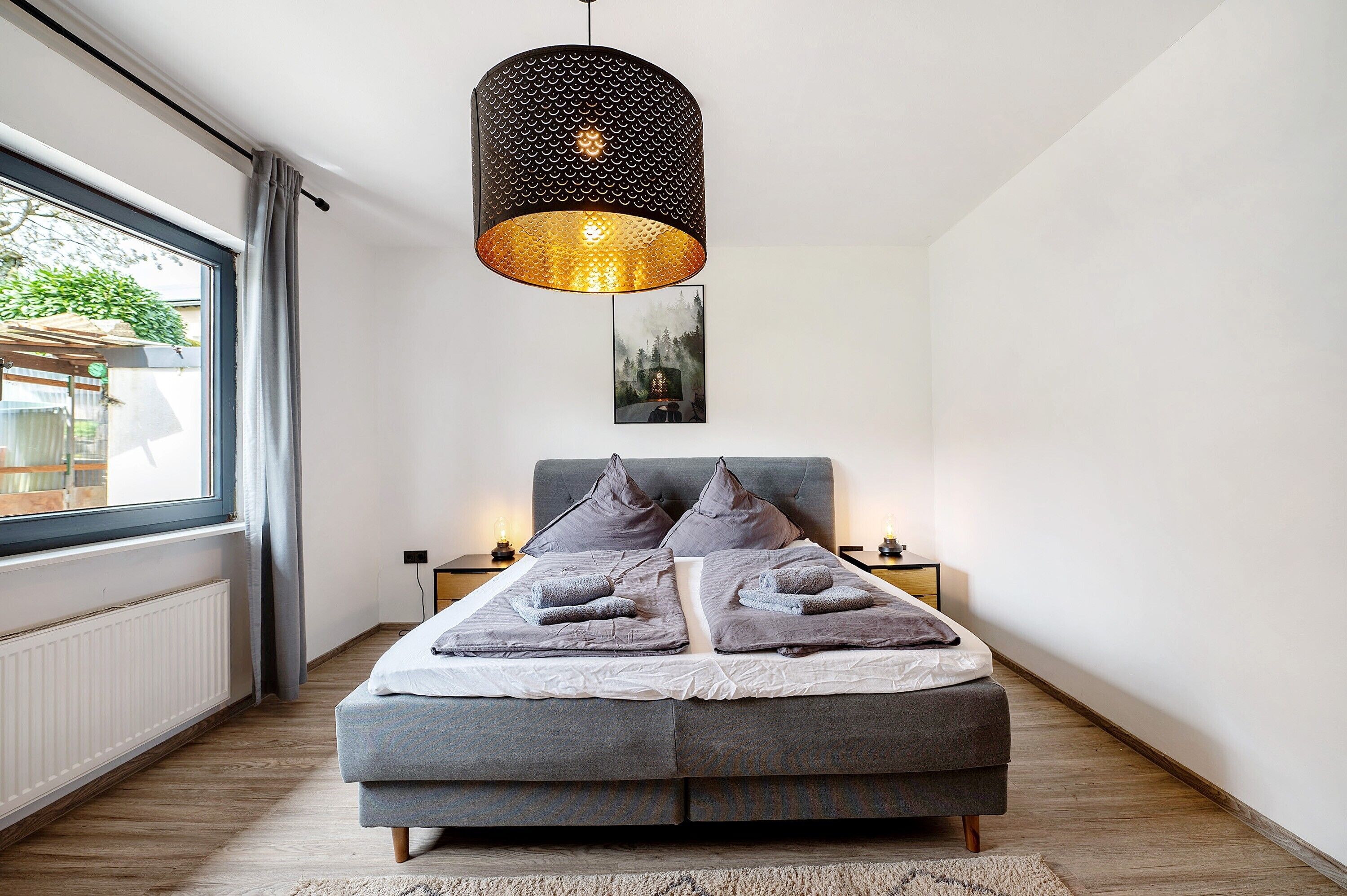 Une chambre à coucher moderne avec un grand lit, une lampe suspendue et une vue sur l’extérieur.