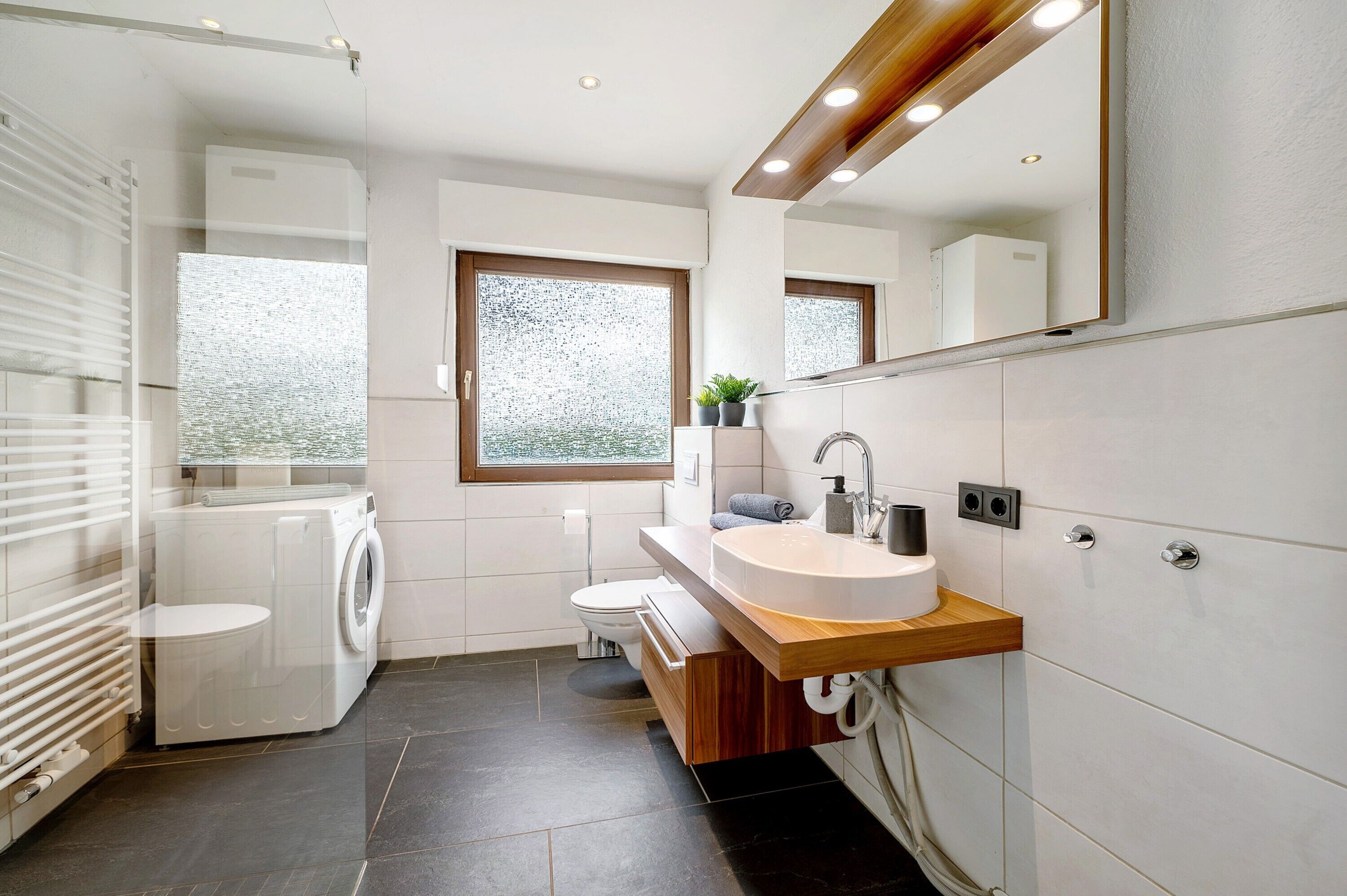 Een moderne badkamer met een wasmachine, toilet, wastafel en grote spiegel.