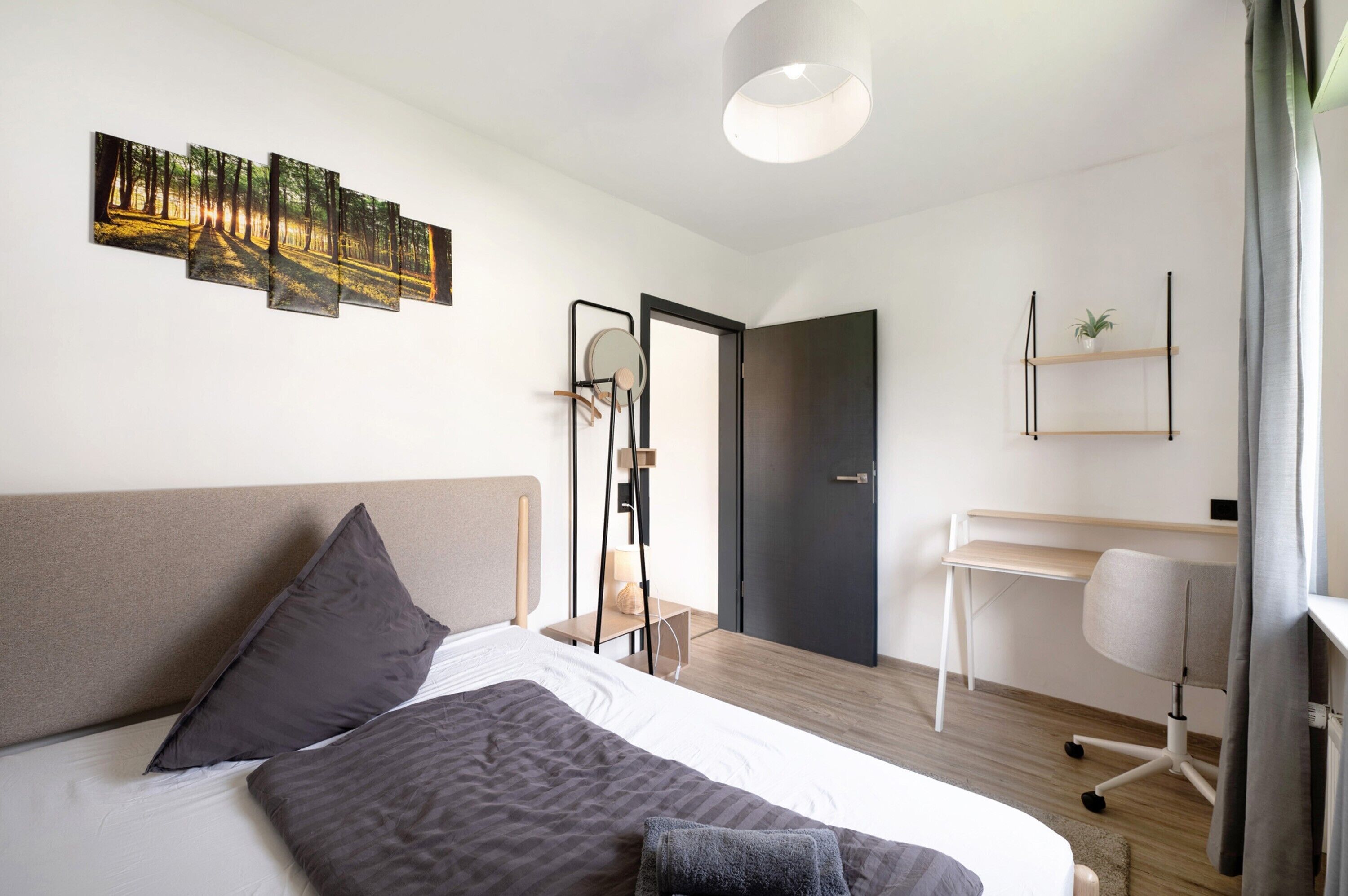 Een moderne hotelkamer met een bed, een bureau, een stoel, een kledingkast en een wanddecoratie.