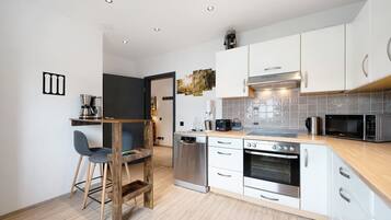 A modern kitchen with white cabinets, stainless steel appliances, and a wooden dining area.