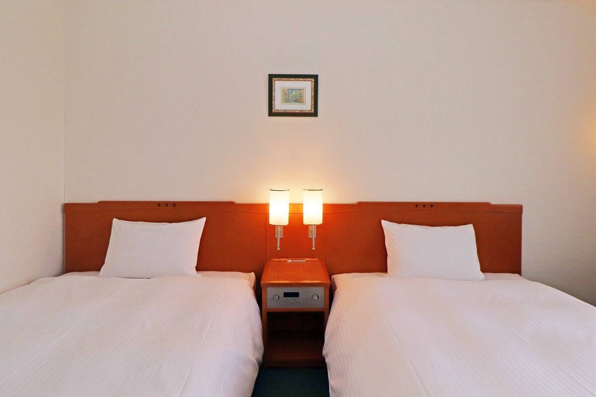 A double room with two beds, each with white linens, a wooden headboard, and bedside lamps.