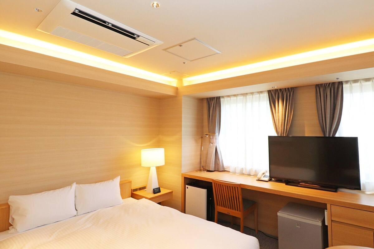 A hotel room with a bed, desk, television, and a small refrigerator.