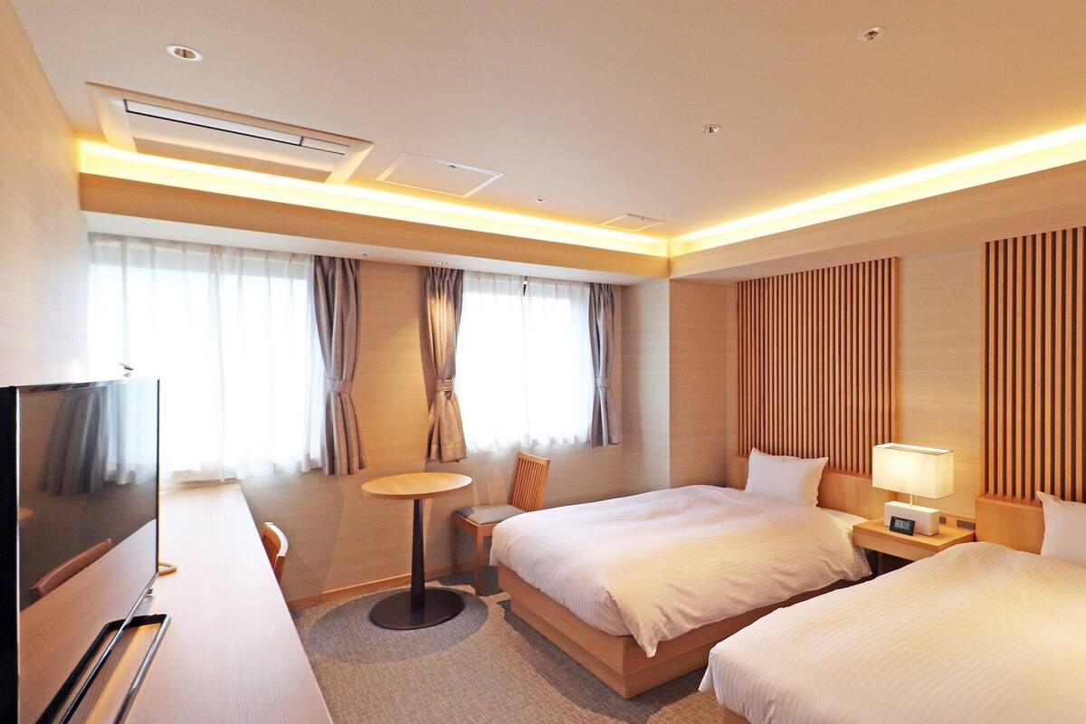 A hotel room with two beds, a TV, a desk, and a small table.