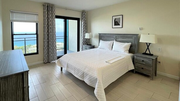 Une chambre à coucher avec un grand lit, une table de chevet, une lampe, une fenêtre donnant sur un beau paysage et un rideau.
