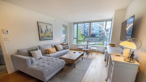 Una sala de estar moderna con un sofá gris, una mesa de centro de madera y un comedor con una pequeña mesa y sillas.