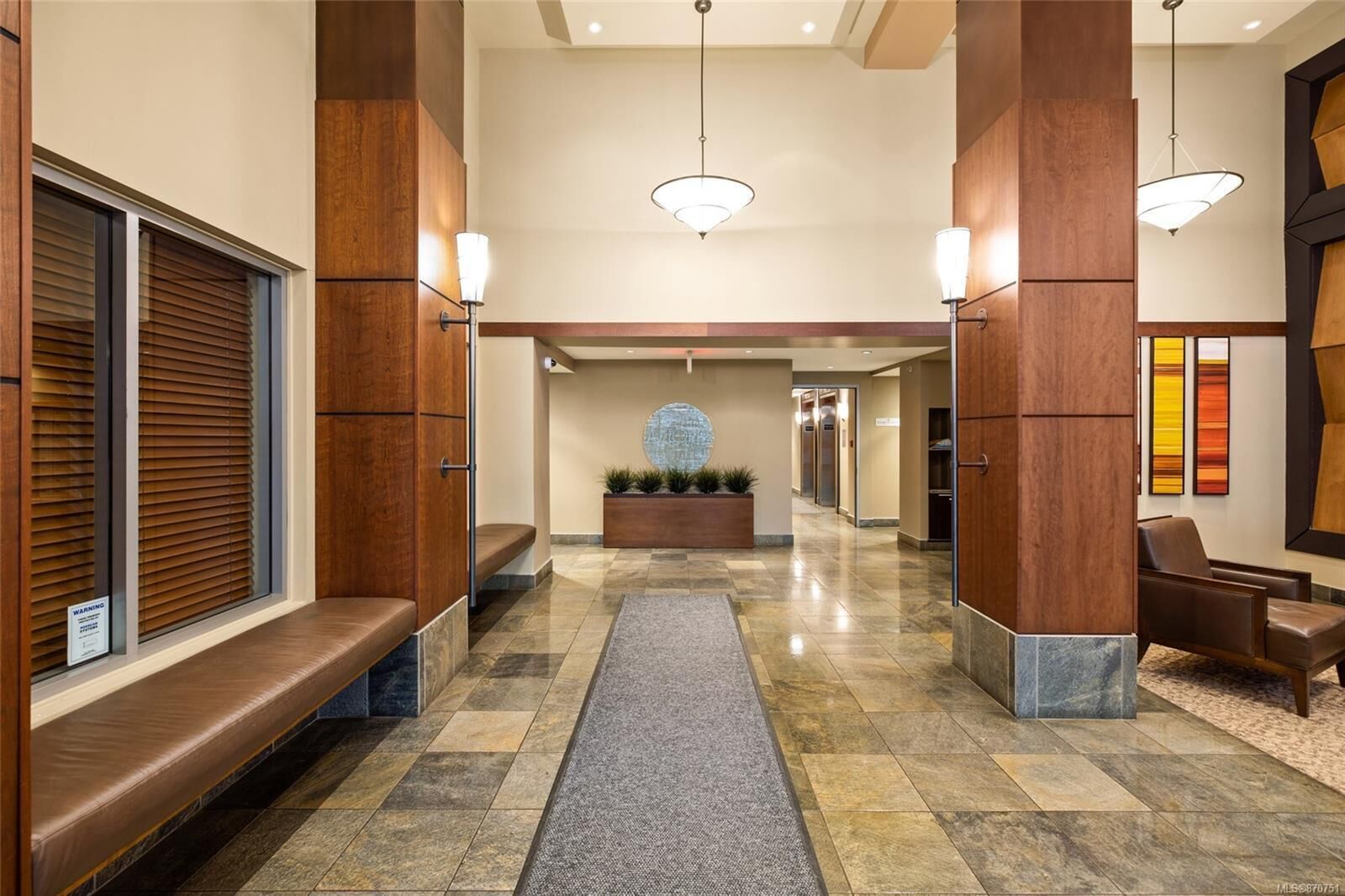 Un vestíbulo de hotel con un mostrador de recepción central, zonas de estar y una pared decorativa con diseño circular.