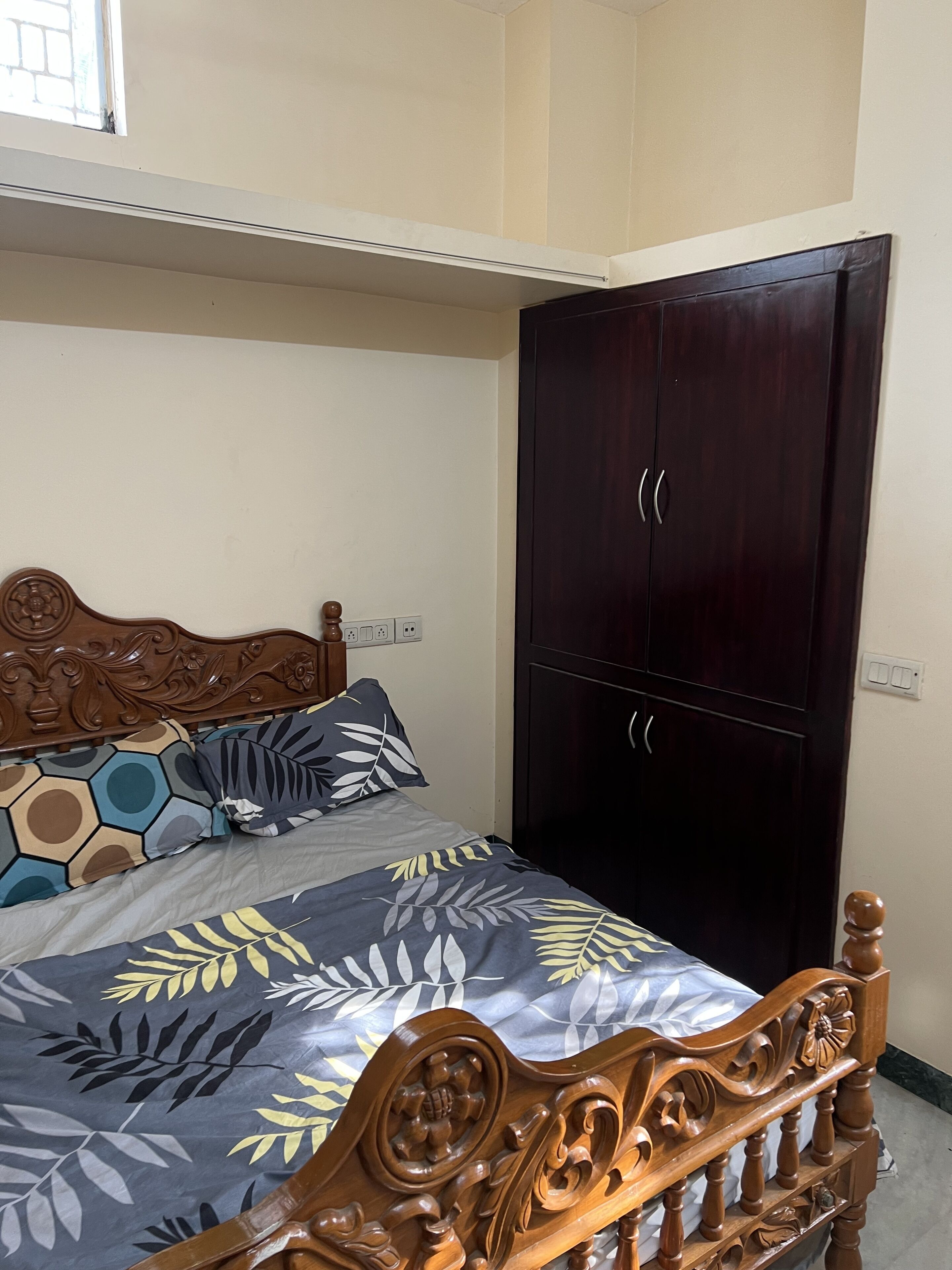 A bedroom with a wooden bed, a dark wardrobe, and a window with a view of the outside.